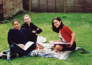 Three St Clare's students studying outside on the grass in the garden