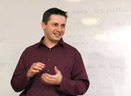 A St Clare's teacher in front of a whiteboard, explaining something with a smile