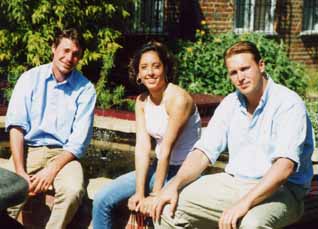 Three young people seated, smiling, in sunlit St Clare's garden