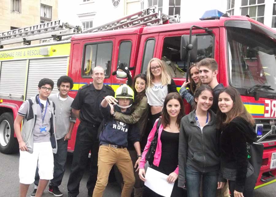 students smiling in front of a fire engine with fire fighter