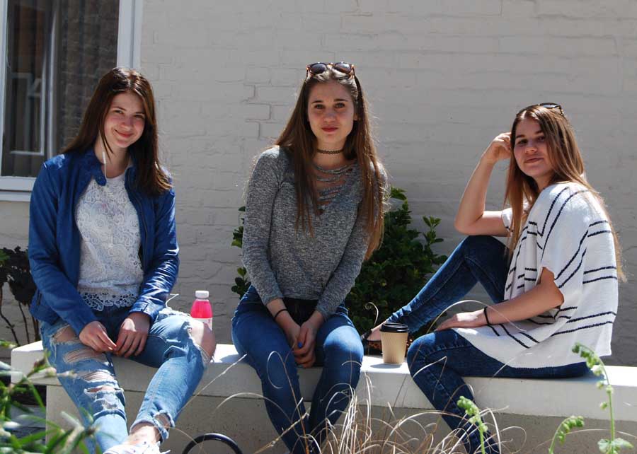 3 teenage girls sitting on the bench in sunshine